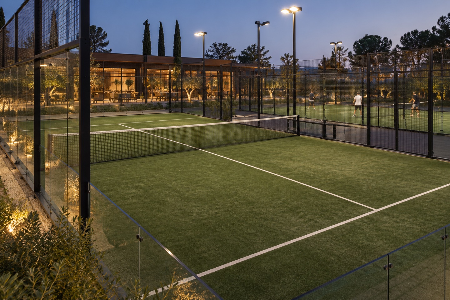 Des terrains de padel éclairés, avec un club-house en arrière-plan.
